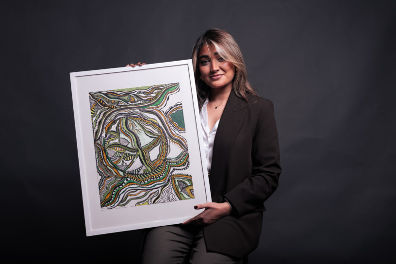 Woman looking upwards on a black background while holding a painting.
