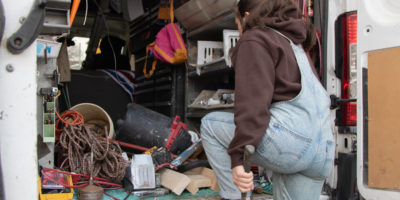 Image of a person holding a hammer and while walking into a truck filled with construction tools.