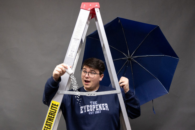 Image of a person under a ladder looking at a salt shaker that has salt pouring out of it while holding a blue umbrella.