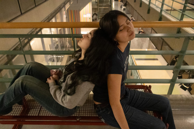 Image of two people leaning against each other sleeping on a bench.