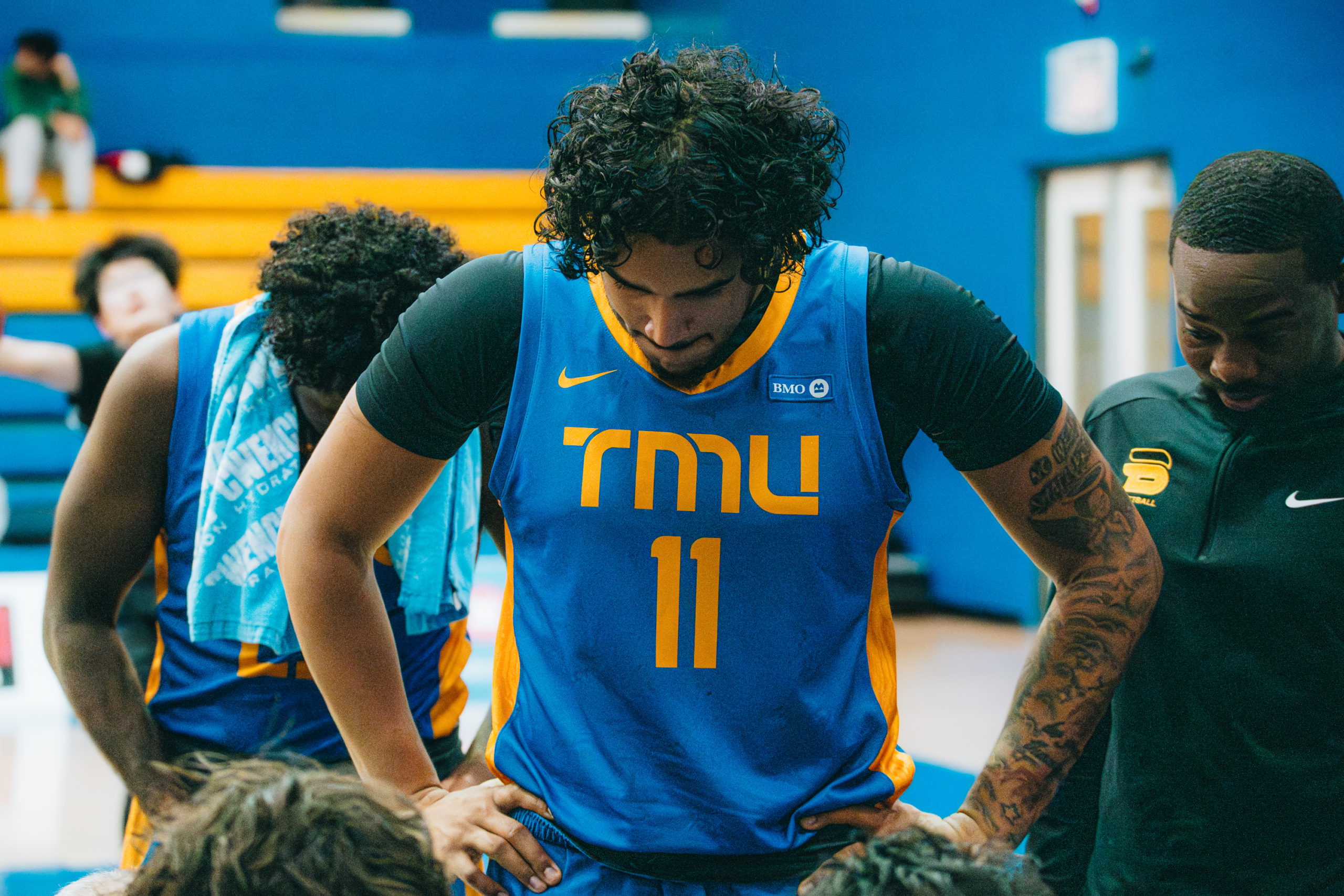 TMU Bold men's basketball team standing over their coach drawing a play at the Mattamy Athletics Centre