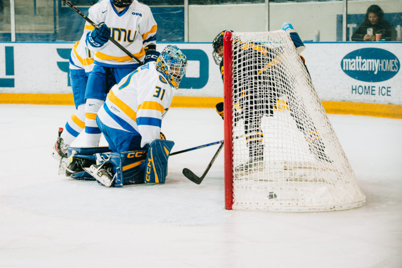 A Waterloo Warriors women's hockey player scoring on the TMU Bold women's hockey team sneaking a goal behind the goalie at the Mattamy Athletics Centre