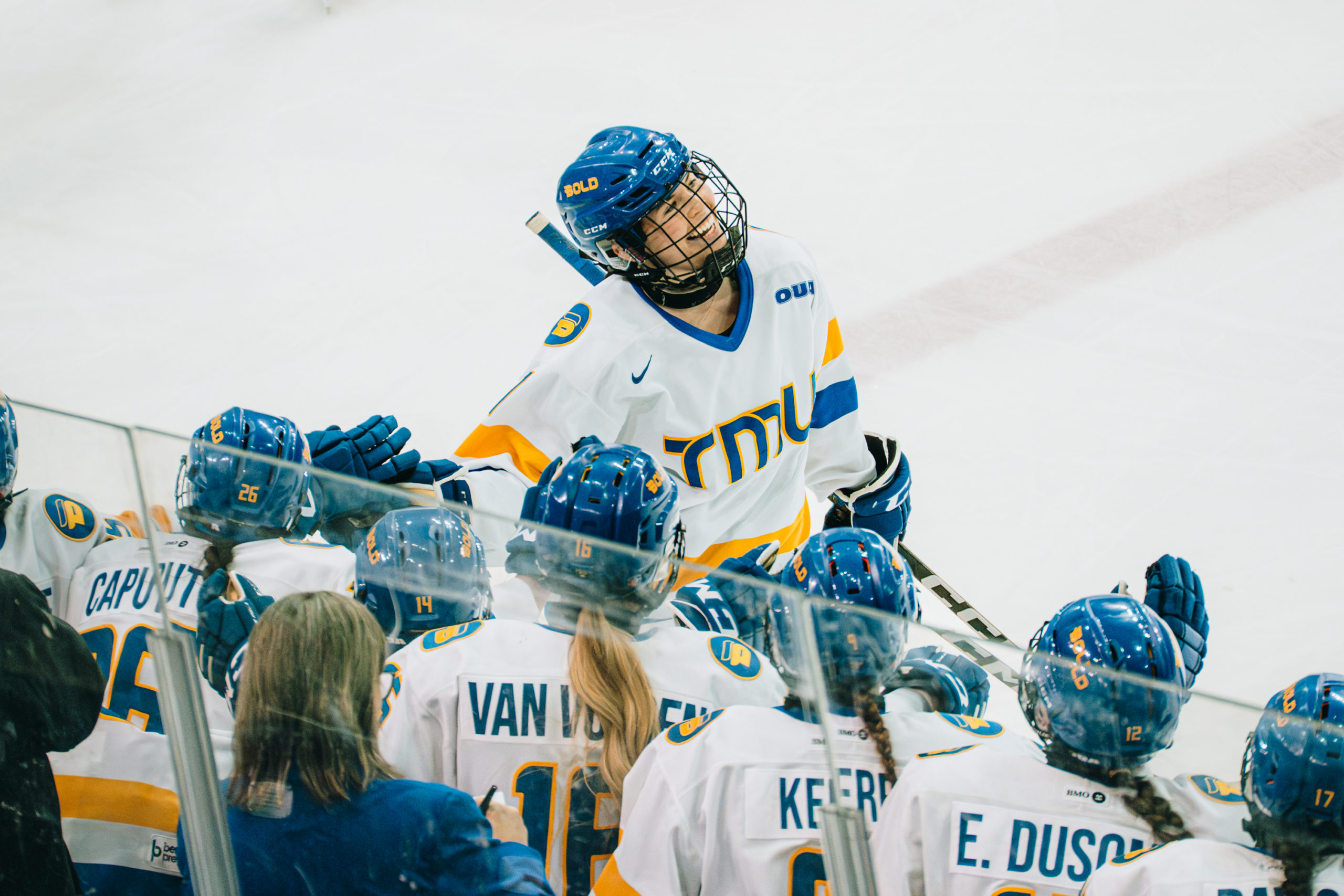 TMU women's hockey player passing the TMU banch with a smile on their face at the Mattamy Athletics Centre