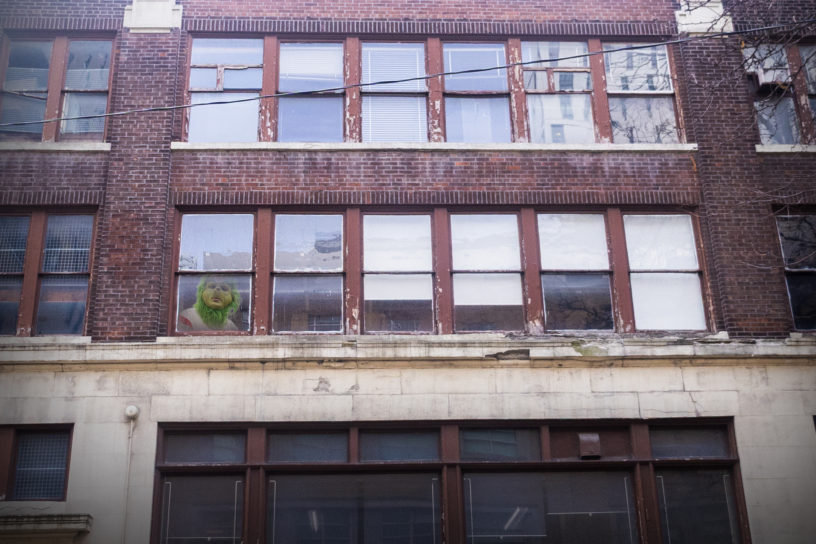 Image of a building with the grinch peeking out of a window from the bottom left side of the frame.