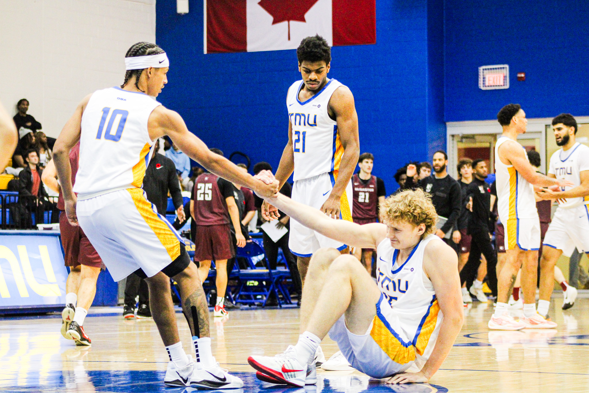 Two TMU Bold mens basketball players helping each other up off the floor