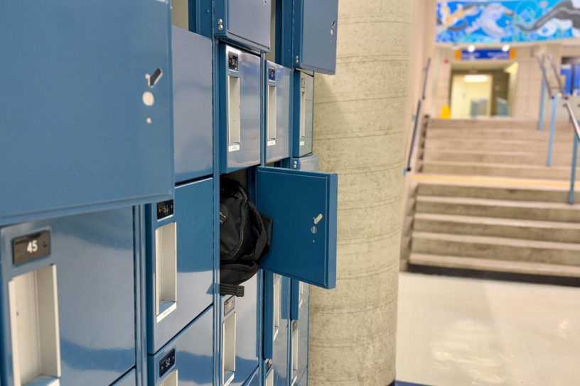 Image of a row of small blue lockers with one open that has a bag sticking out.