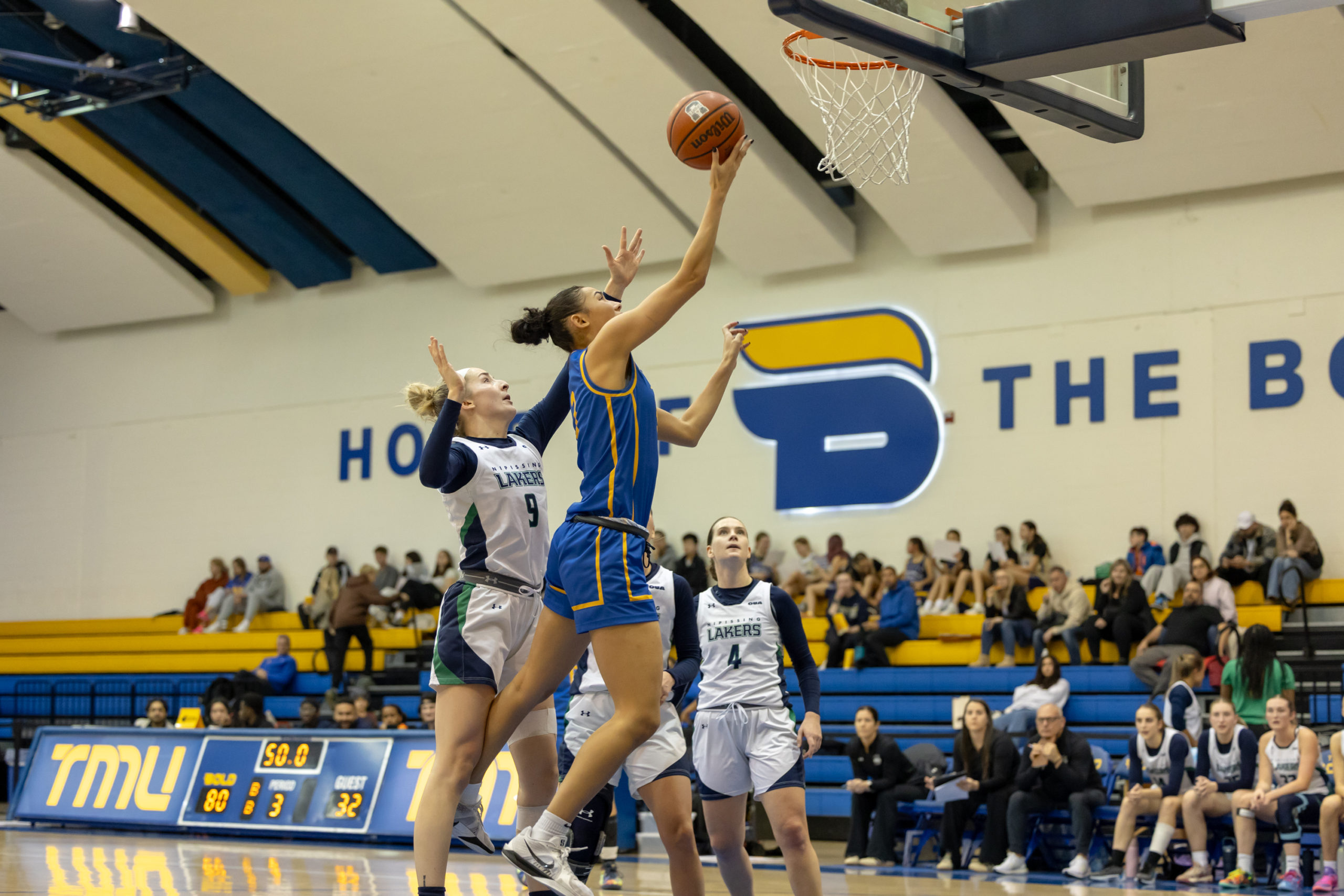 A TMU player reaches for the basket amidst Nipissing defense