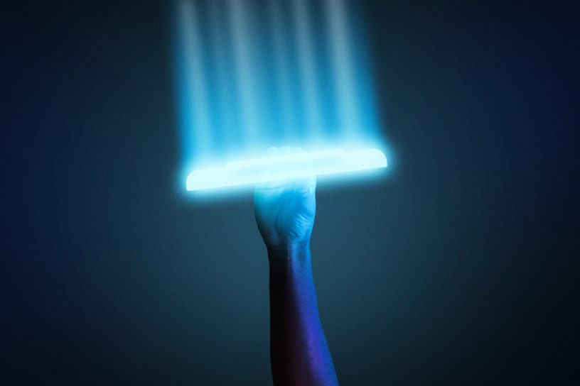 A arm is holding up a frisbee that is glowing blue against a dark background.