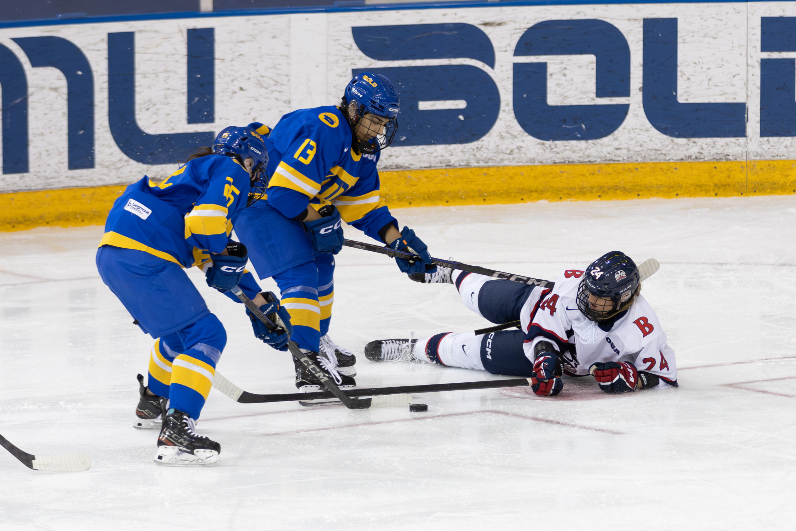 Two TMU Bold women's hockey players defending a grounded Brock offensive player at Mattamy Athletic Centre