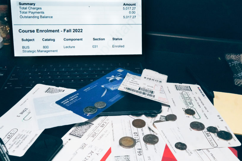 Image of travel tickets, foreign money and a computer with tuition costs open on the screen.
