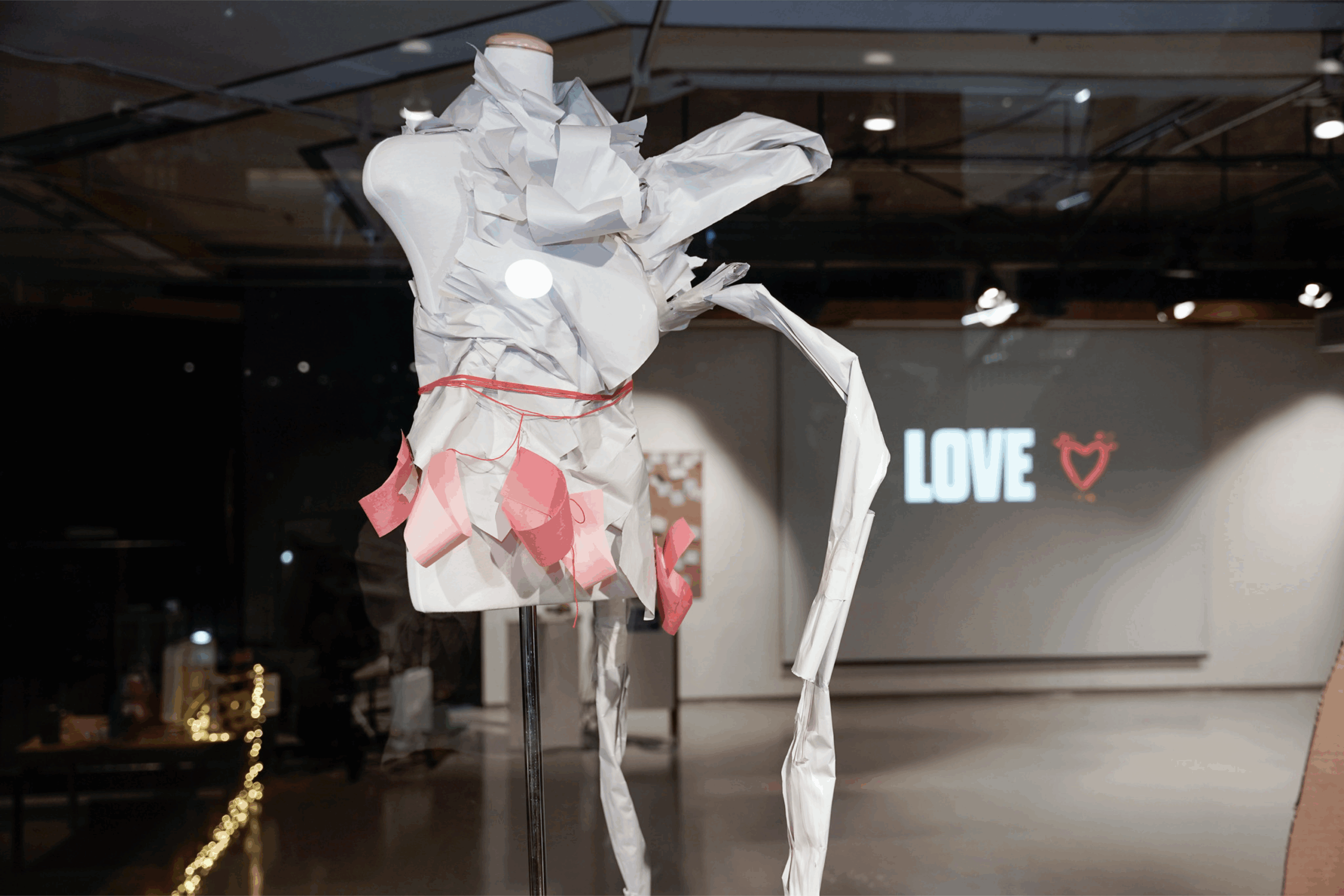 An abstract, mannequin-like sculpture stands in the middle of an art gallery.