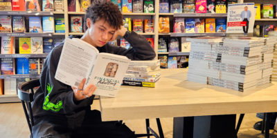 Image of a person reading a book titled "Financial Adulting" as they lean against a stack of books.
