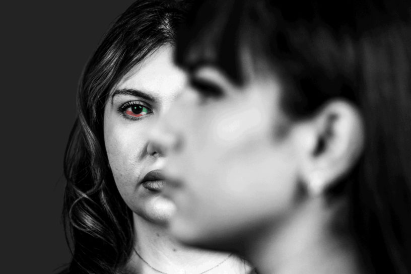 Black and white photo of two people, one facing the left and one facing forward with the colors of the Iranian flag in their eye