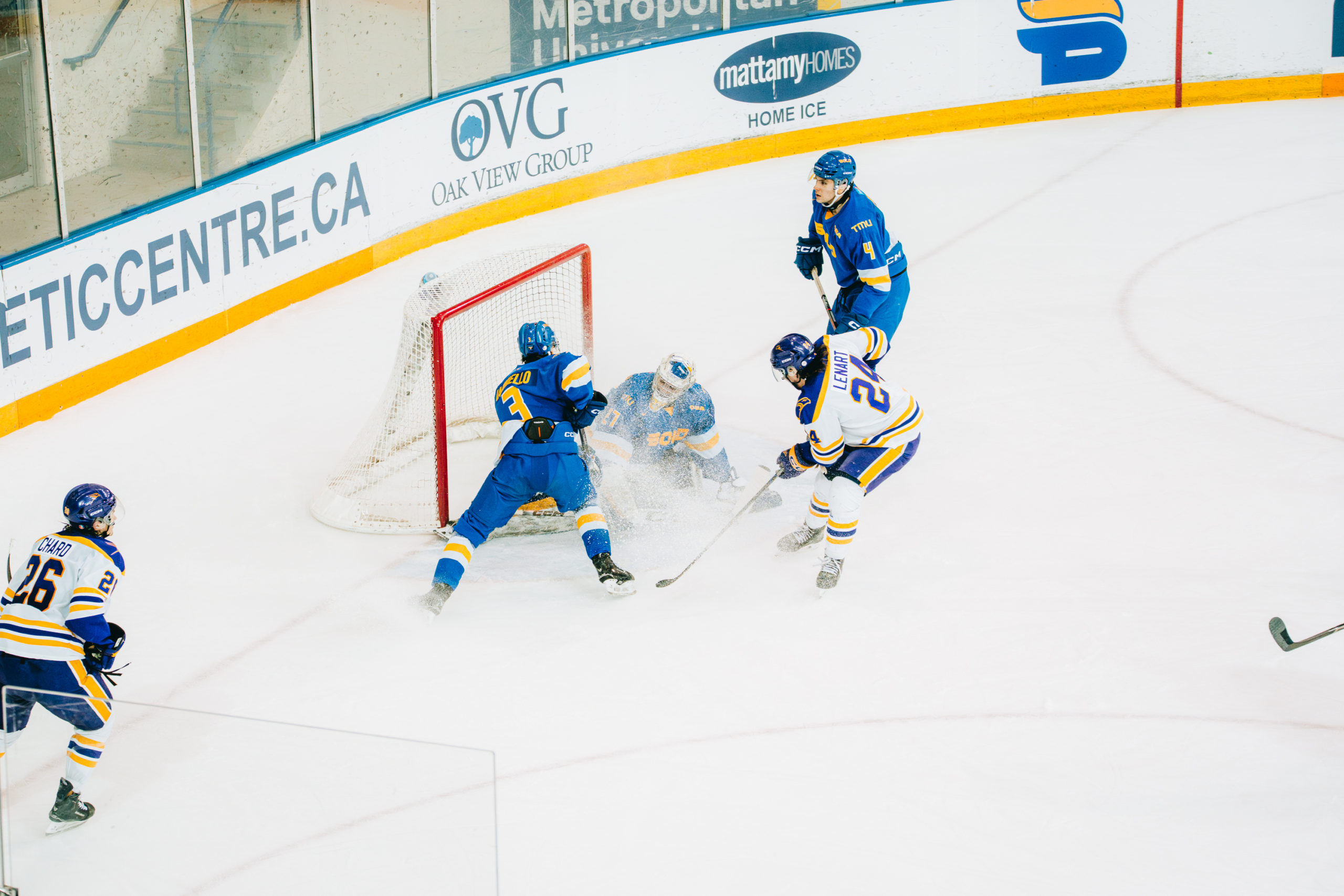 A TMU men's hockey player battles at the net against a Laurier player at the net at the Mattamy Athletic Centre
