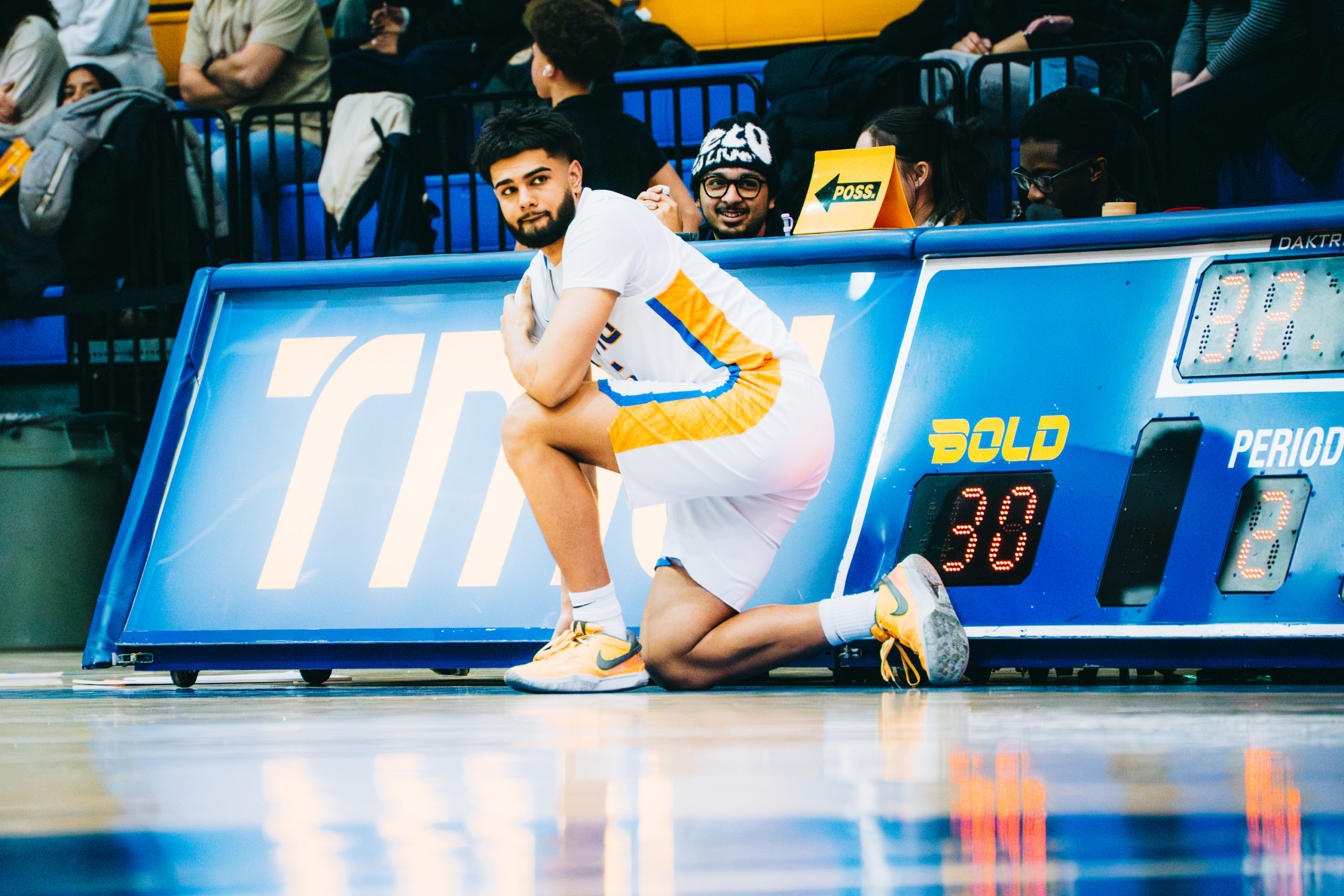 A TMU player kneels court-side, preparing to be substituted in