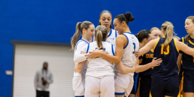 TMU women's basketball group together in a hug on the Mattamy Athletic Centre court