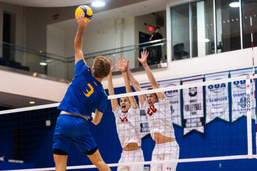 A TMU player sends a kill down the net and past two RMC blockers 