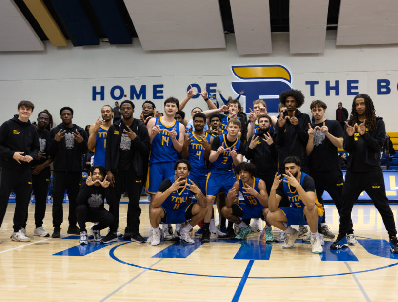 TMU bold men's basketball team comes together for a group photo after a win against Brock in the 2026 OUA playoffs