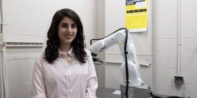 An image of Haniyeh Altafi standing next to a robotic arm.