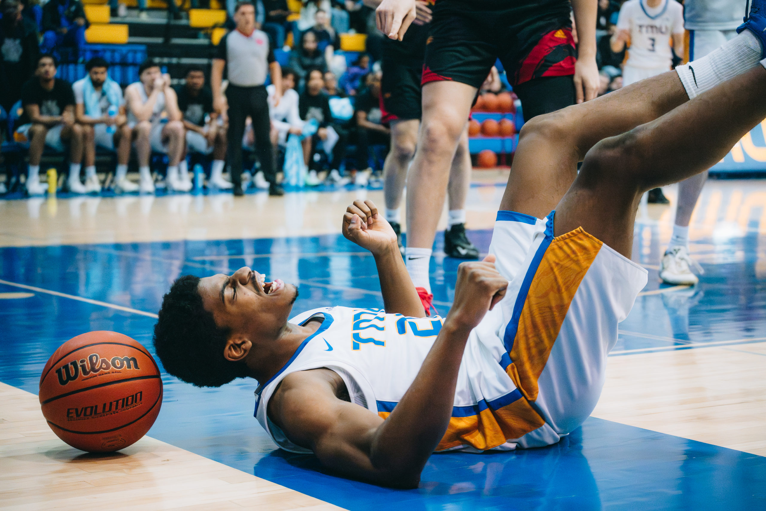 A TMU Bold men's basketball player on his back on the ground after a play 