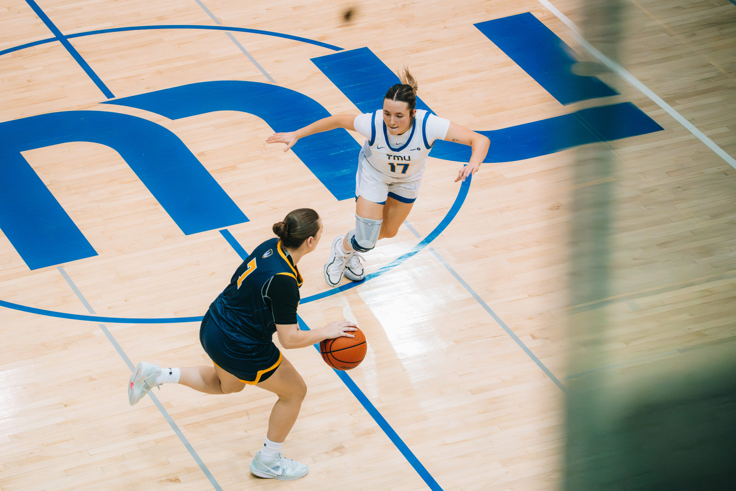 A TMU and Windsor player face each other centre-court, the TMU player hoping to defend as Windsor maintains possession