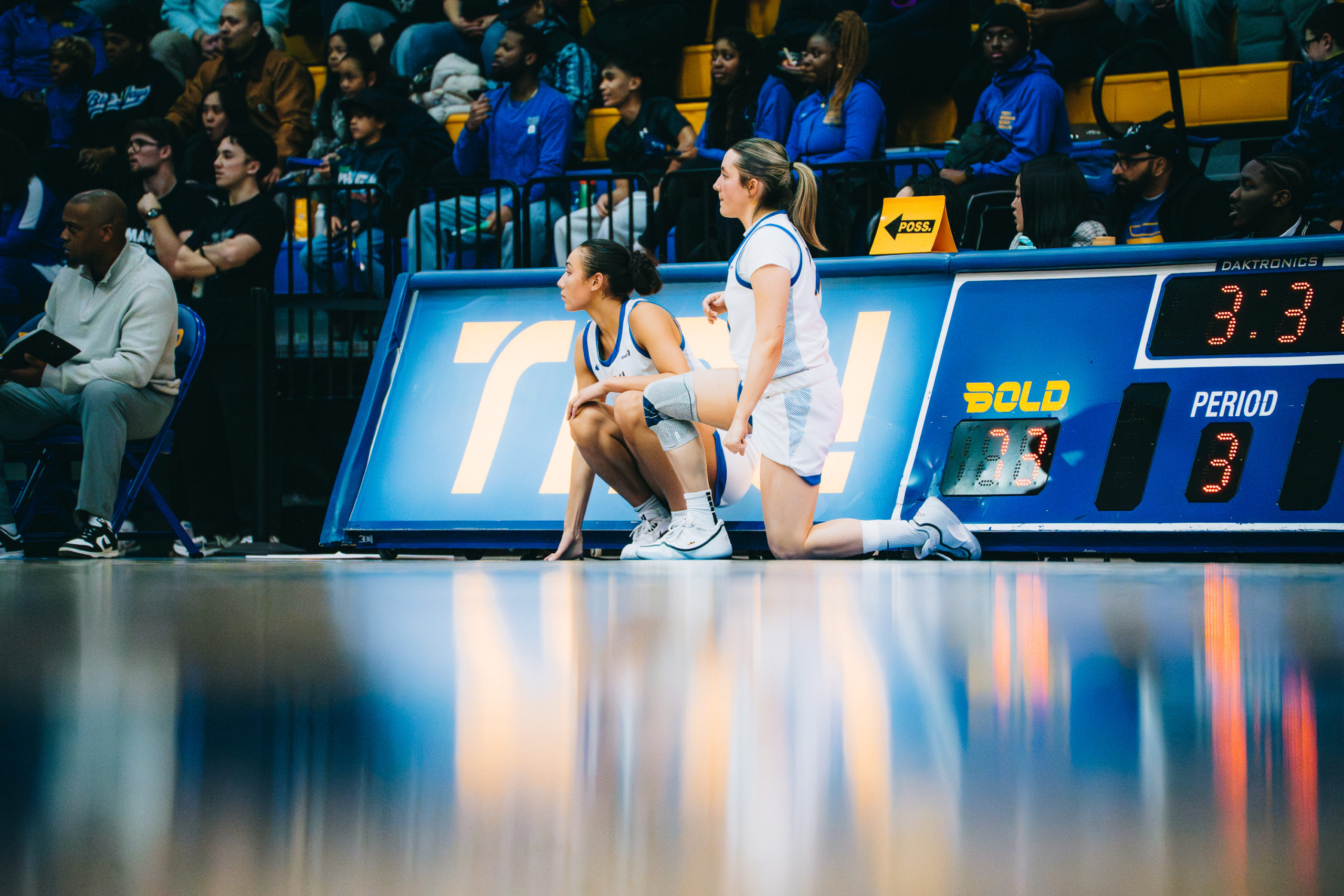 Two TMU players kneel court-side, preparing to be substituted in