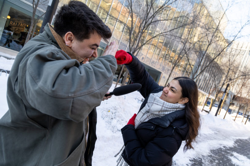 A girl punches a boy holding a microphone outside.