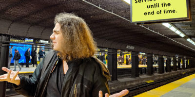 Someone standing on the TTC platform with their arms out in a confused matter. The board reads, "Service delayed until the end of time" behind them.