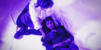 A young person is embraced by their friend as they lie down on their lap.