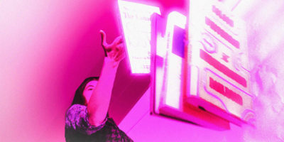 A person throws books onto the floor, an ominous pink light is casted over the image.