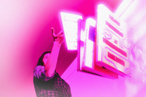 A person throws books onto the floor, an ominous pink light is casted over the image.