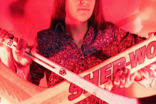 A person stands in front of two hockey sticks.