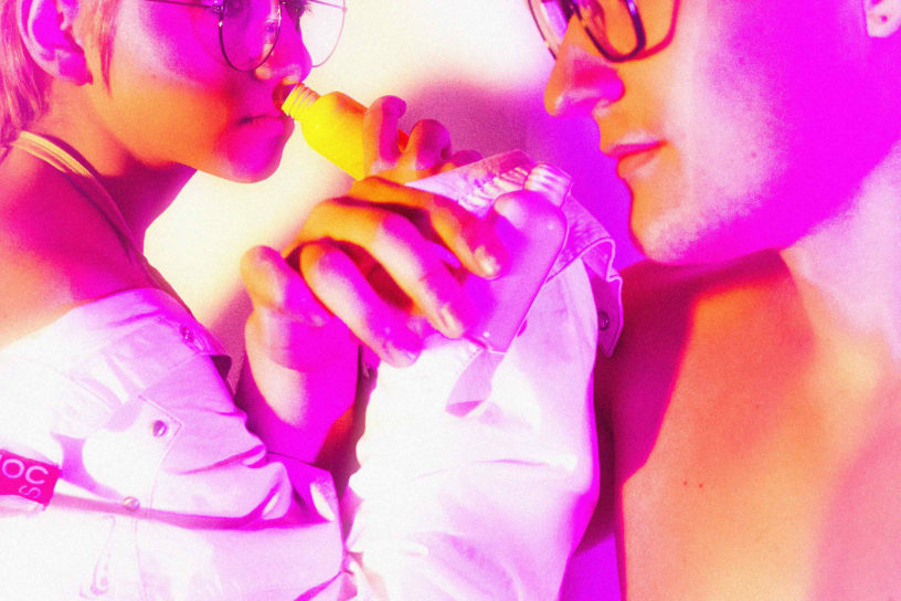 Two people have arms interlinked and inhaling from small bottles.