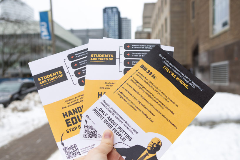 Stack of Bill 33 flyers being held up outside on TMU campus.