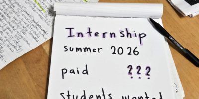 A notepad sits over a wooden table, with the words “internship summer 2026” and other notes written over it
