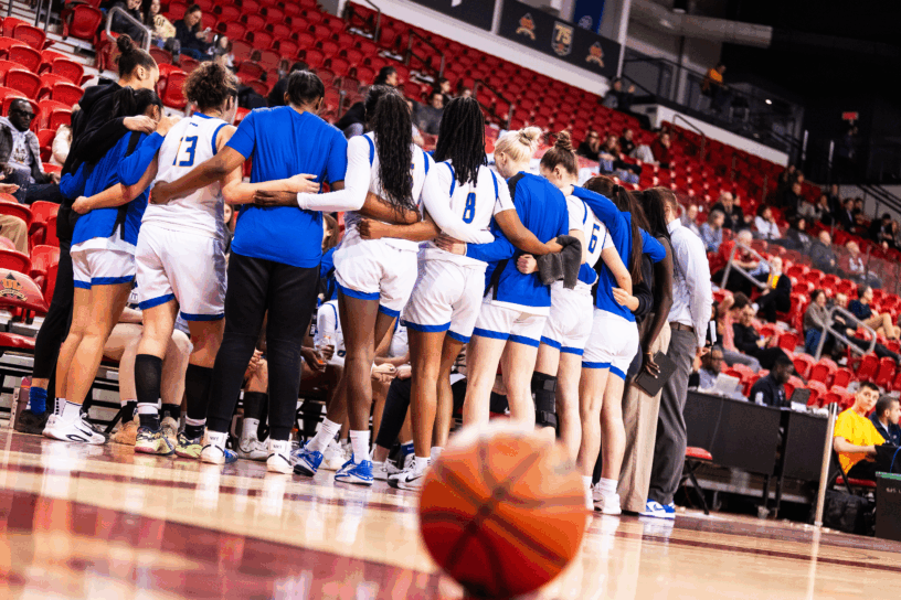 A basketball sits on the court as TMU huddles around their bench