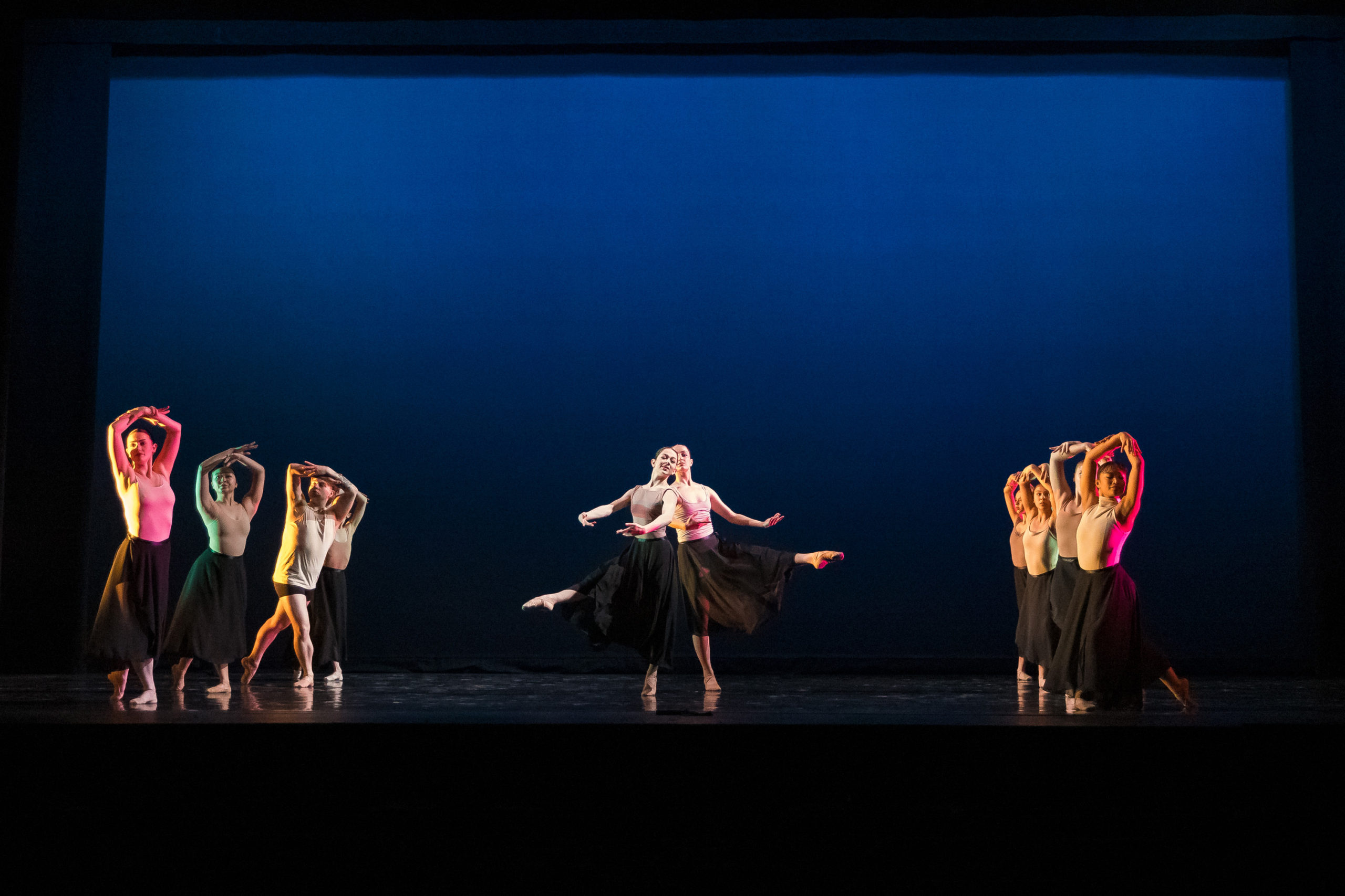 A group of dancers performing ballet in front of a blue background.