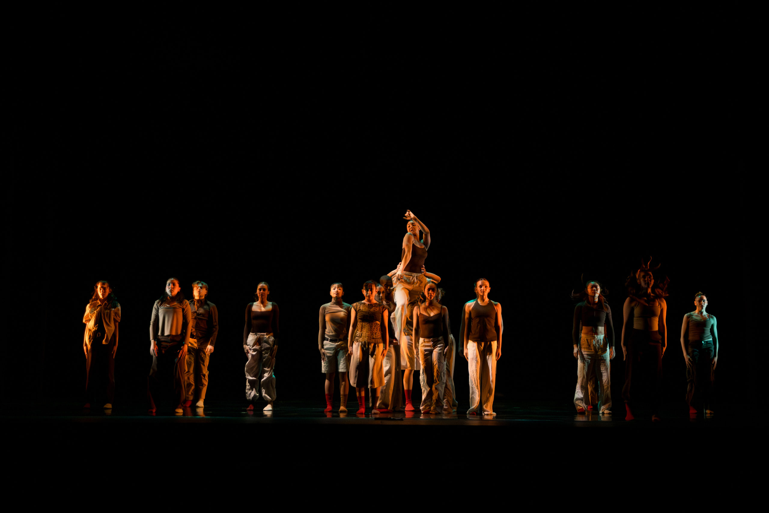 A group of dancers perform a lift with warm lighting hitting them.