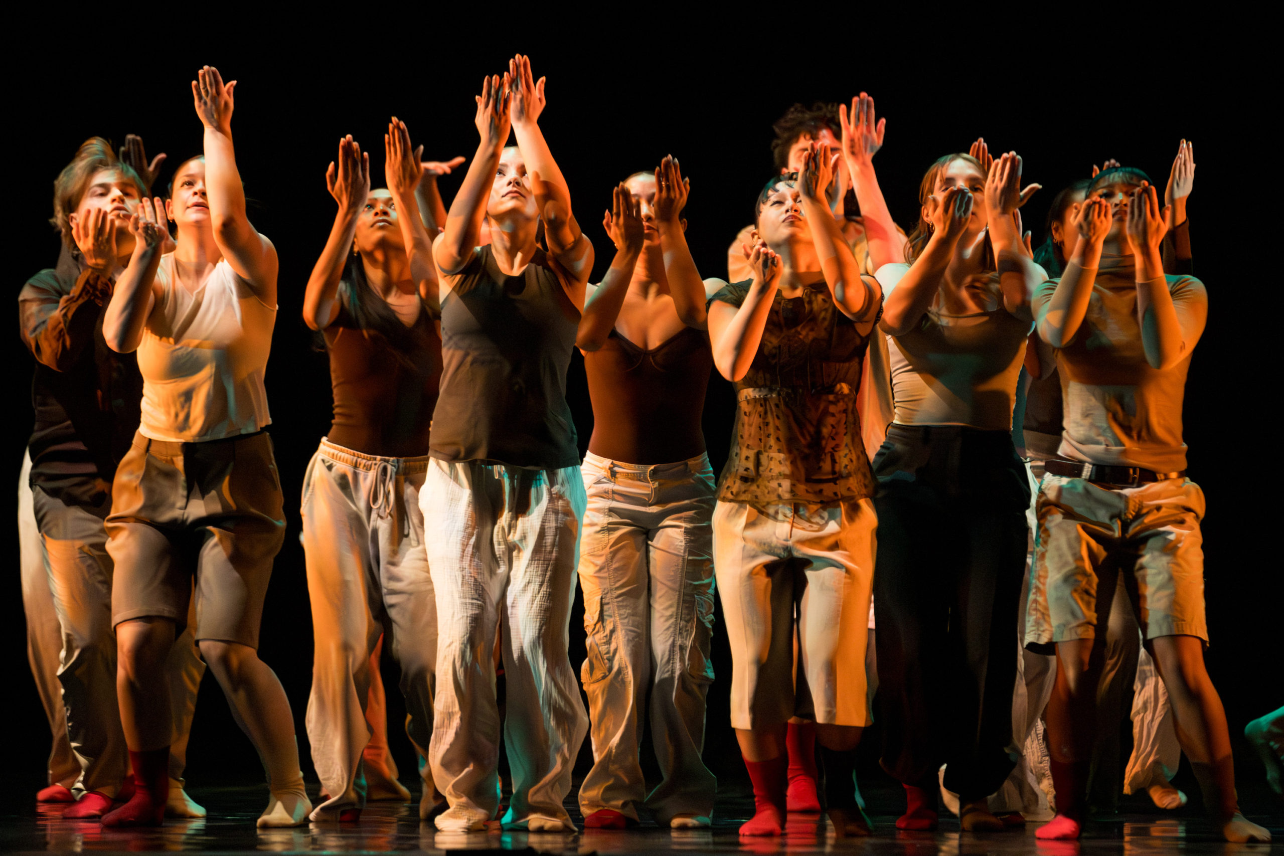 A group of dancers performing with their arms up, warm lighting is hitting them.