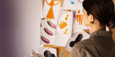 A woman holds a clipboard and studies a cork board full of images of eggplants, ties and a briefcase.