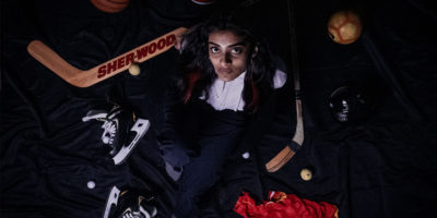 Photo of a woman looking upwards, while surrounded with various sport equipment on a black background.