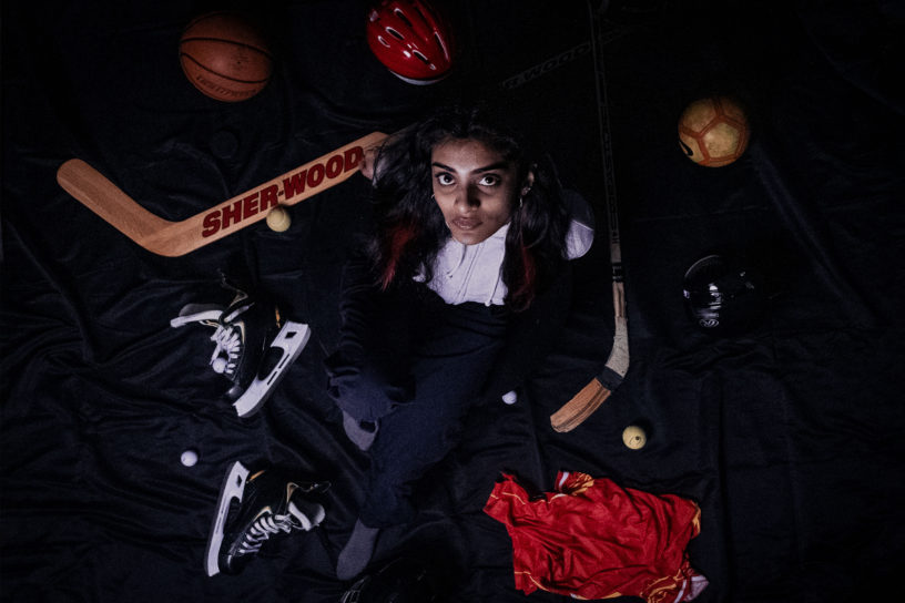 Photo of a woman looking upwards, while surrounded with various sport equipment on a black background.