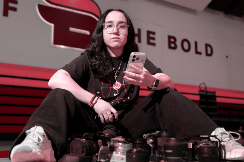 Chrysoula Dimitrakopoulos sitting on a basketball court with a bunch of cameras below her.