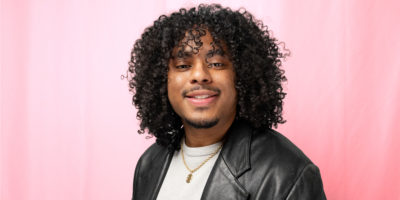 A photo of a man in a black leather jacket, smiling in front of a red backdrop.