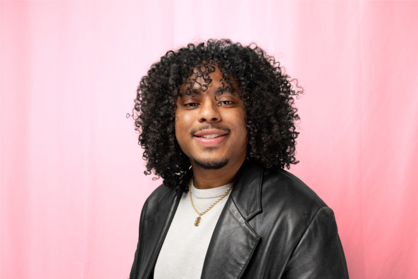 A photo of a man in a black leather jacket, smiling in front of a red backdrop.
