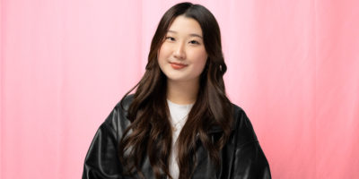A photo of a woman in a black leather jacket, smiling in front of a red backdrop.