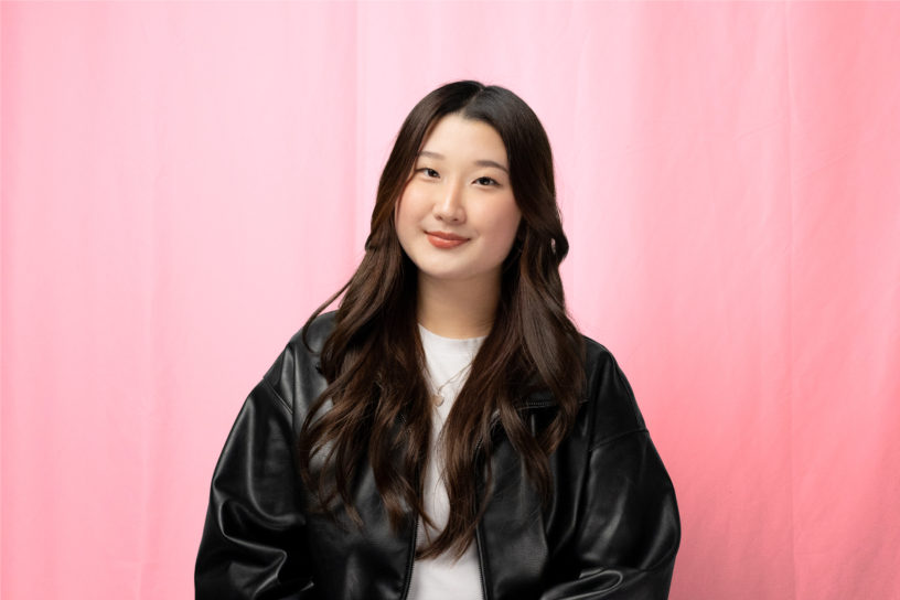 A photo of a woman in a black leather jacket, smiling in front of a red backdrop.