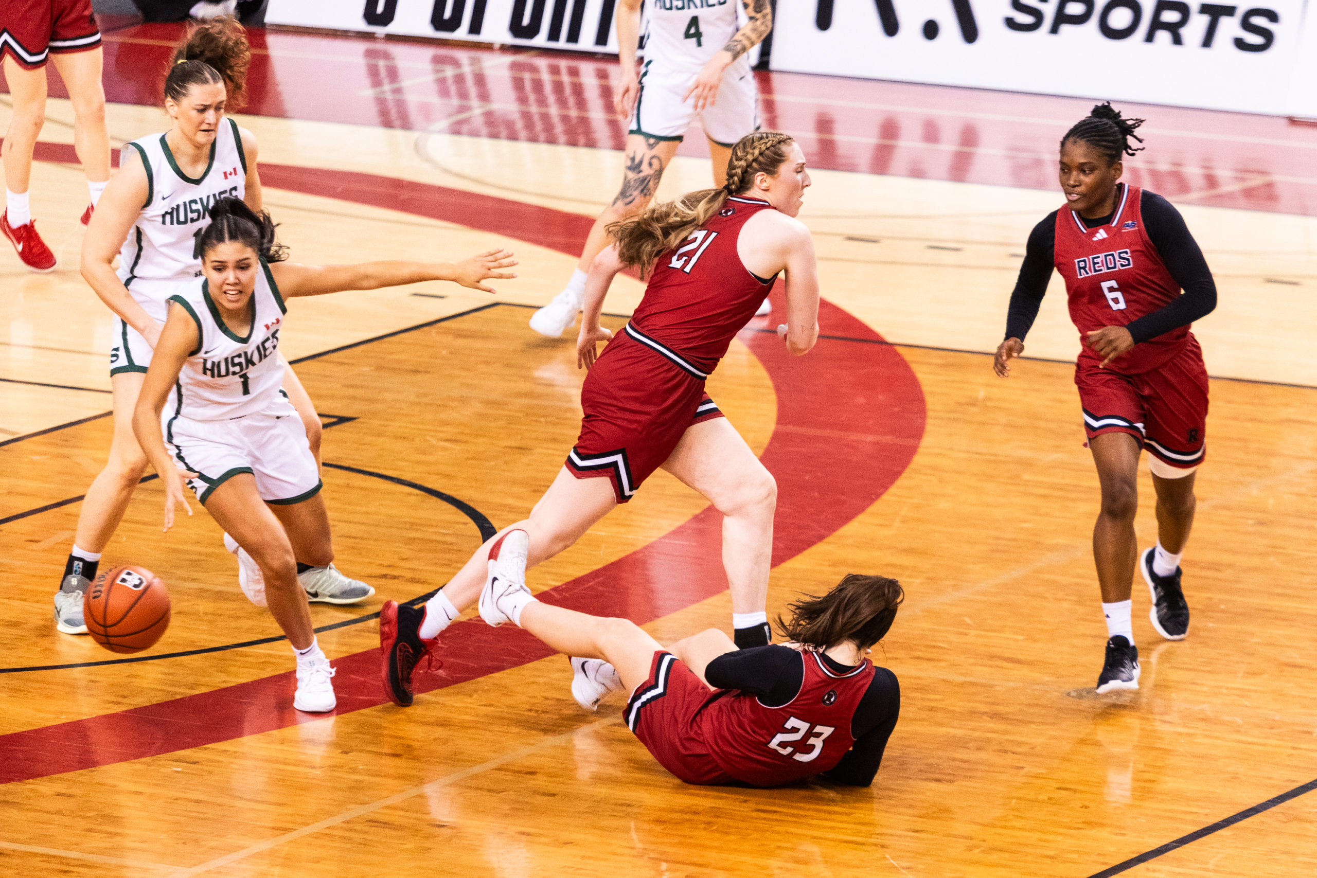 A Huskies player gains possession as Reds player rush to protect their side of the court