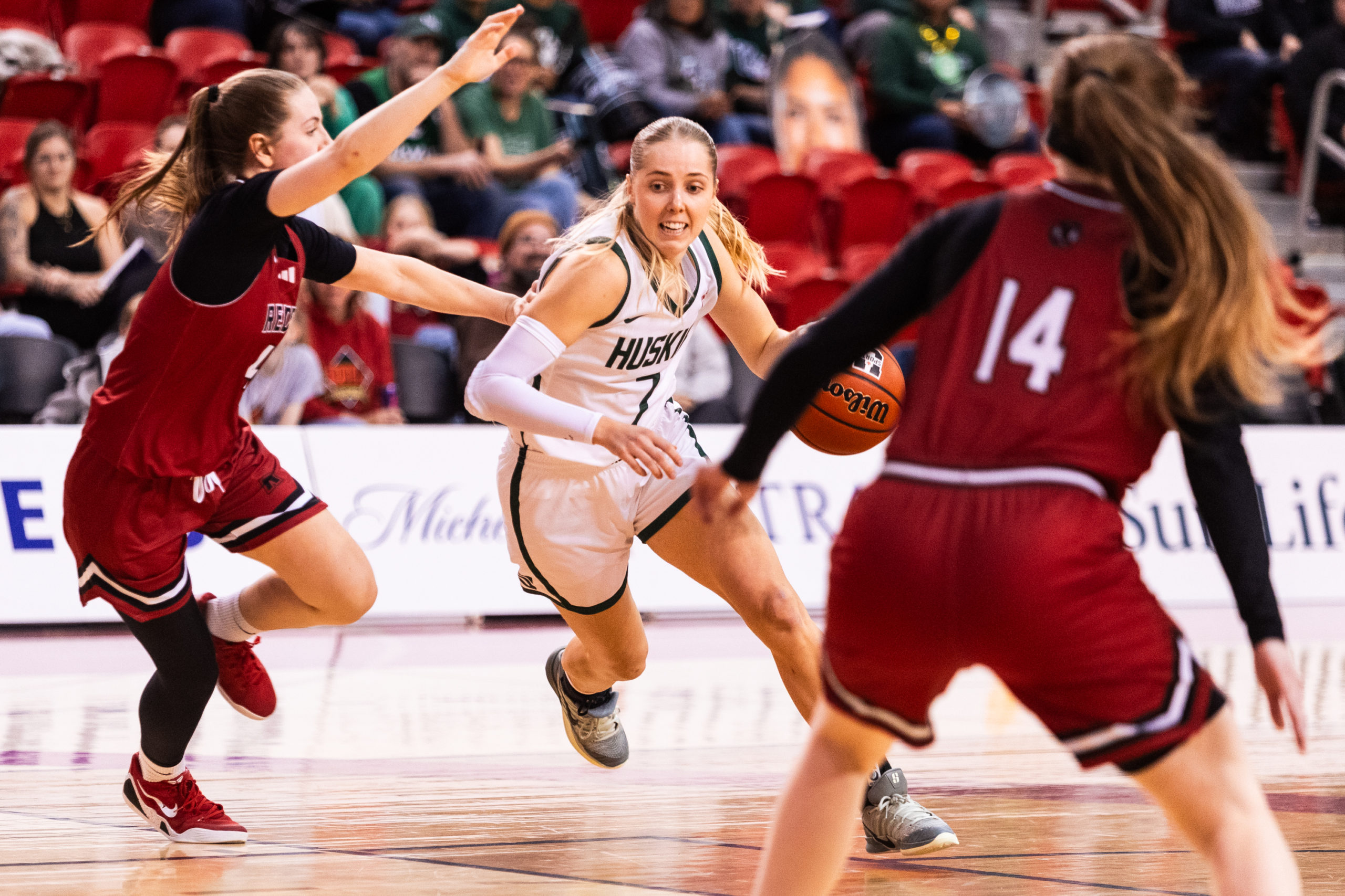A Huskies player maintains possession amidst multiple Reds opponents trying to block her