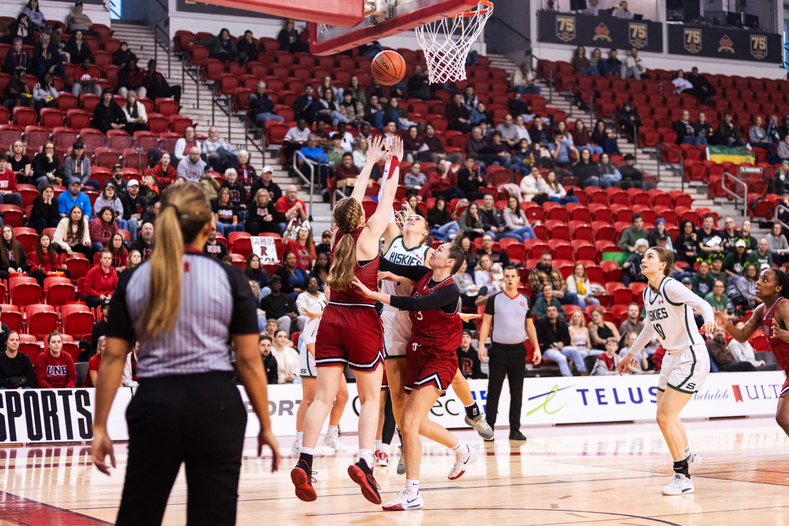 A Huskies player makes a shot as Reds players try to keep the ball from getting into the basket
